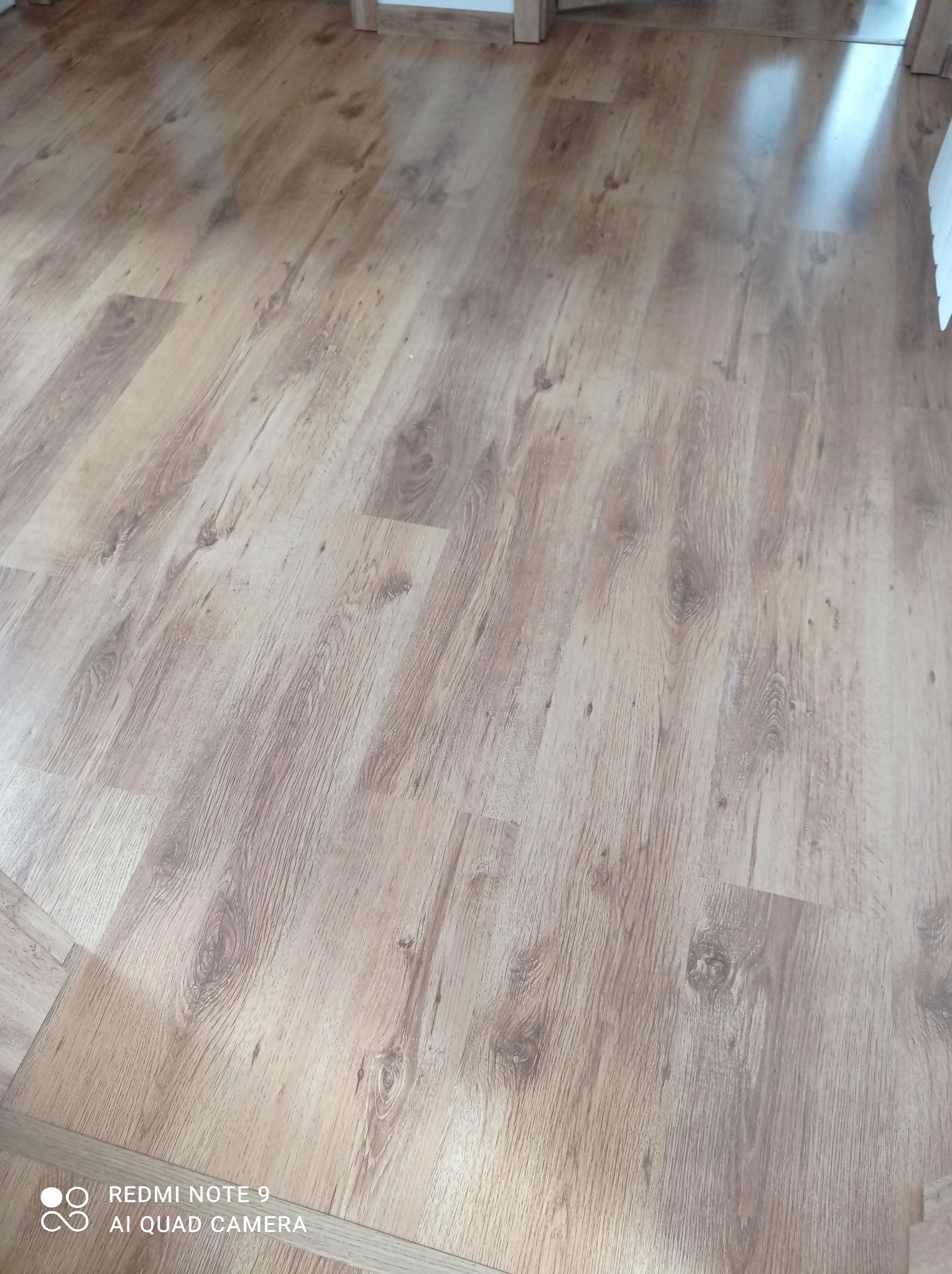 Ułożona podłoga z paneli imitujących jasne drewno, widoczne słoje i faktura, z delikatnym połyskiem.