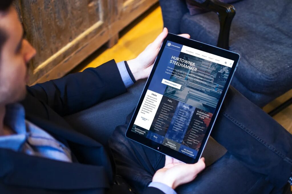 Mężczyzna w garniturze przegląda na tablecie stronę internetową hurtowni stali Steelhammer, siedząc w fotelu.
