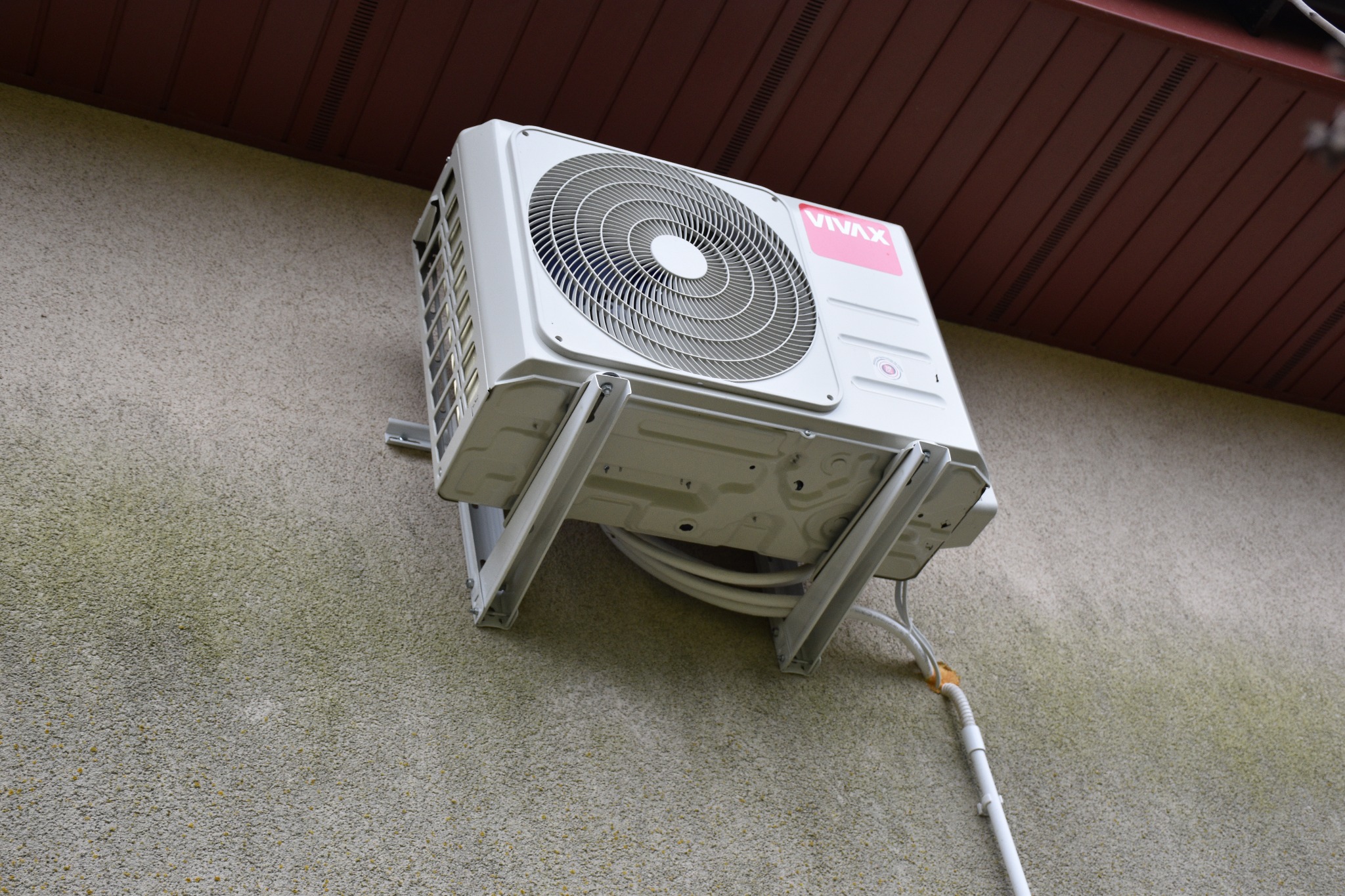 Zewnętrzna jednostka klimatyzacji marki Vivax, zamontowana na elewacji budynku z widocznymi przewodami i elementami montażowymi.