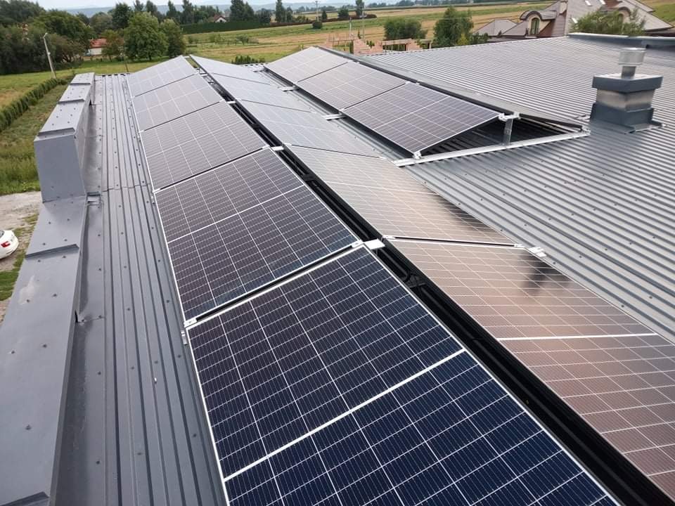 Panele słoneczne zamontowane na szarym metalowym dachu domu jednorodzinnego, widok z góry, z kominem w tle.