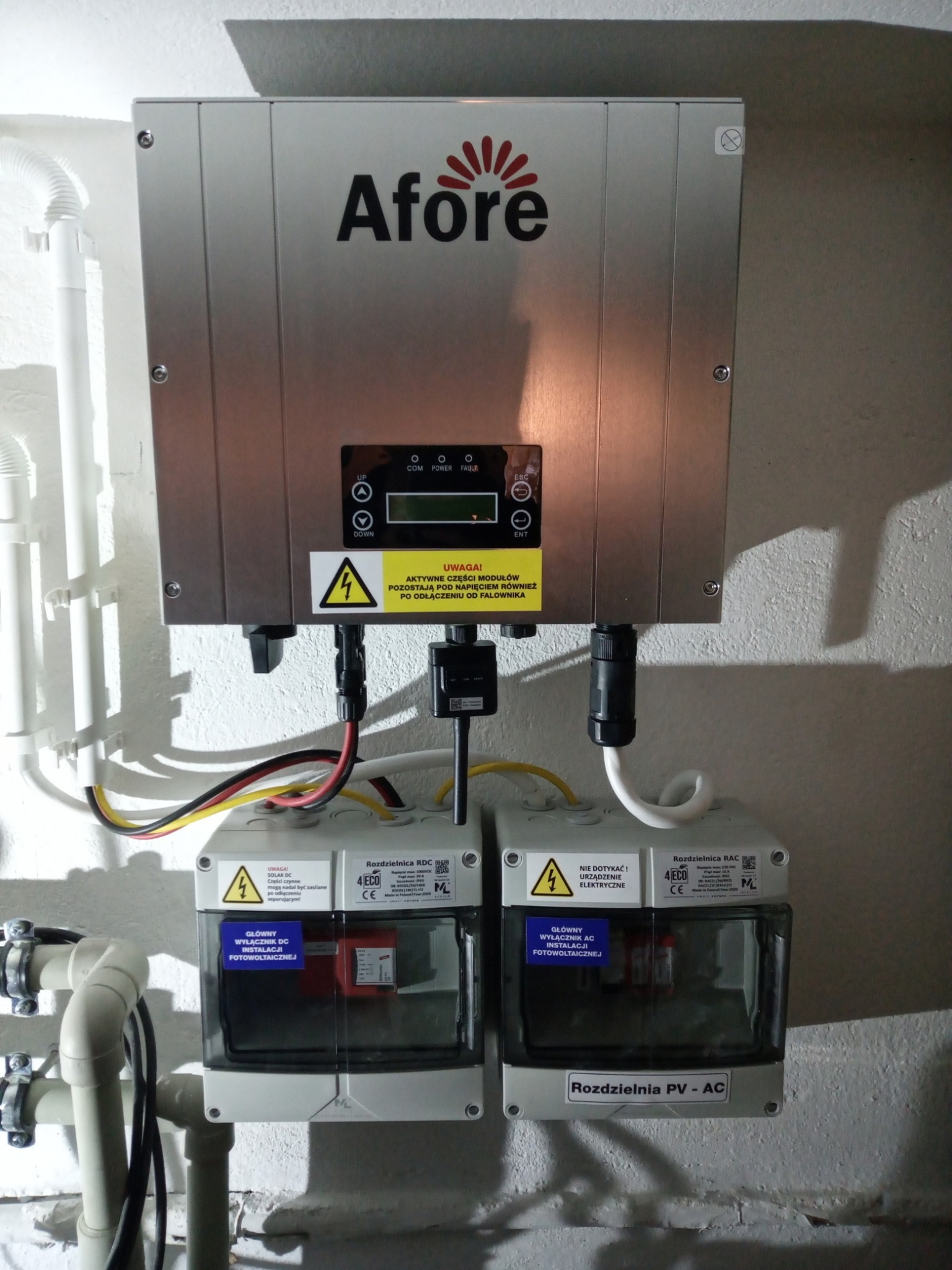Falownik Afore z rozdzielnicami RDC i RAC na ścianie, widoczne przewody i ostrzeżenia o napięciu elektrycznym, instalacja fotowoltaiczna.