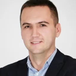 Portret uśmiechniętego mężczyzny w garniturze na jasnym tle.