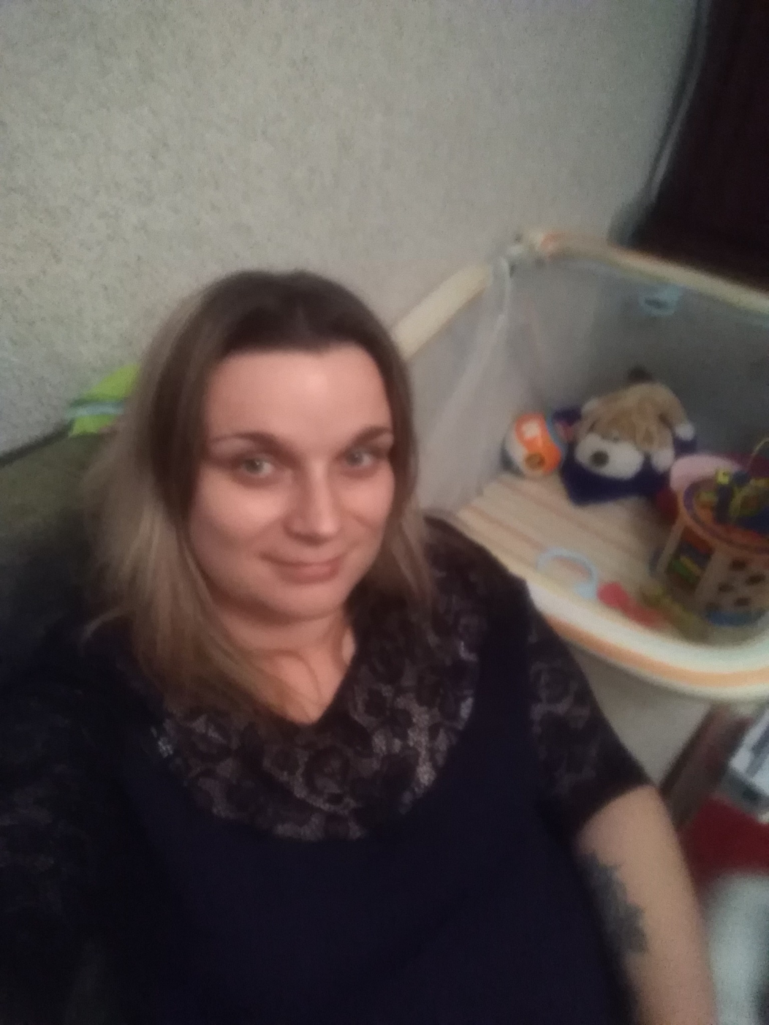 Kobieta z blond pasemkami pozuje na tle łóżeczka dziecięcego wypełnionego zabawkami.