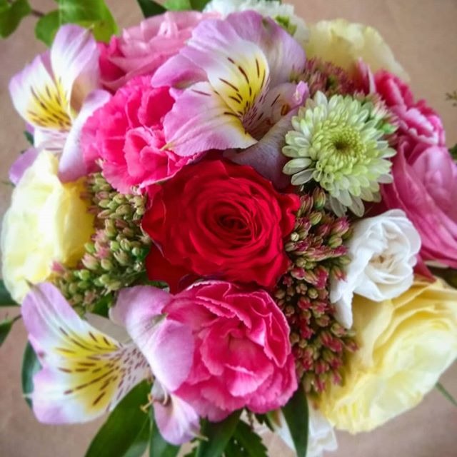 Bukiet mieszany z róż, alstromerii, goździków i chryzantem w odcieniach różu, czerwieni, żółci i bieli, z zielonymi dodatkami, widok z góry.