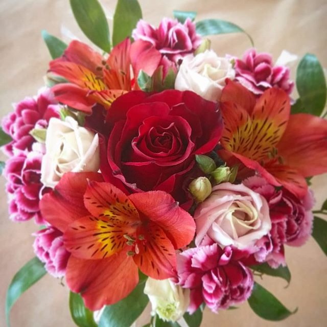 Kompaktowy bukiet z czerwonych róż, alstremerii i różowych goździków, ułożony na jasnym tle.