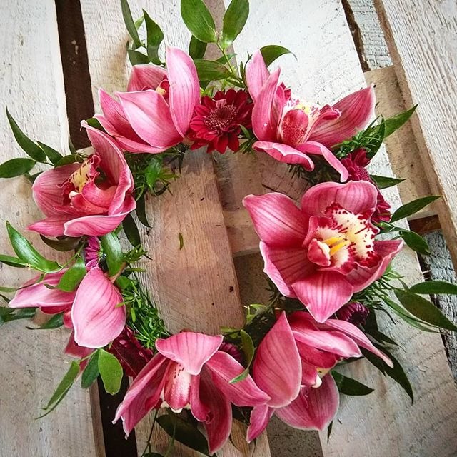 Dekoracyjny wieniec z różowych orchidei i ciemnoczerwonych astrów na tle drewnianych desek w stylu rustykalnym.