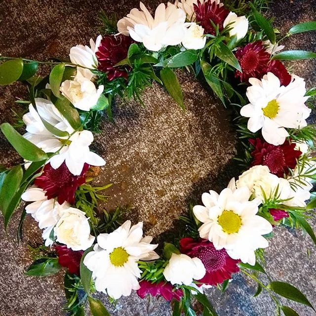 Okrągły wieniec z białych i bordowych kwiatów oraz zielonych liści, wykonany przez florystę z Bydgoszczy, ułożony na szarym, teksturowanym tle.