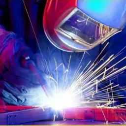 Spawanie metalowych elementów konstrukcyjnych z intensywnym blaskiem iskier, widoczna maska i rękawice ochronne.