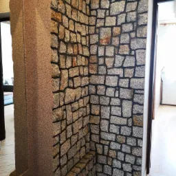 Dekoracyjna ściana z kamienia wewnątrz domu w Słopnicach, widoczne połączenie z ścianą pokrytą tapetą strukturalną.