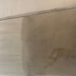 Częściowo wyczyszczona, beżowa tapicerka kanapy z widocznymi plamami i wyraźną różnicą w kolorze po praniu. Widoczny efekt czyszczenia tapicerki.