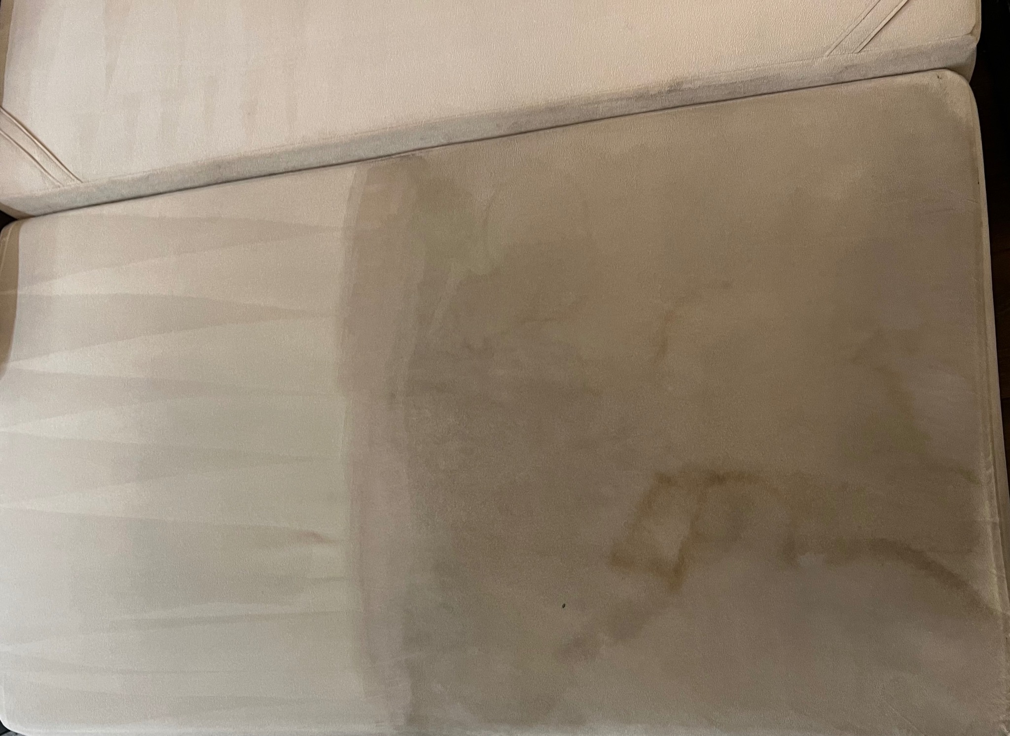 Częściowo wyczyszczona, beżowa tapicerka kanapy z widocznymi plamami i wyraźną różnicą w kolorze po praniu. Widoczny efekt czyszczenia tapicerki.