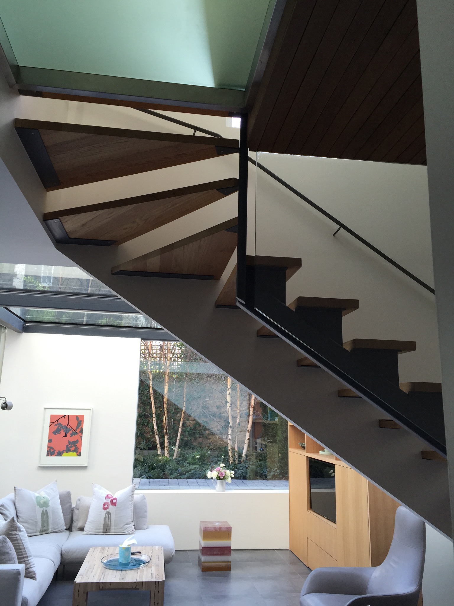 Nowoczesne schody z drewnianymi stopniami i metalową konstrukcją w jasnym wnętrzu z dużym oknem na ogród.