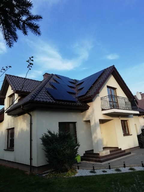 Dom jednorodzinny z zamontowanymi panelami słonecznymi na dachu, widok z poziomu gruntu w słoneczny dzień.