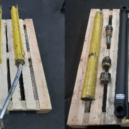 Hydrauliczne cylindry: dwa żółte, używane, i dwa czarne, po renowacji, leżące na drewnianej palecie.