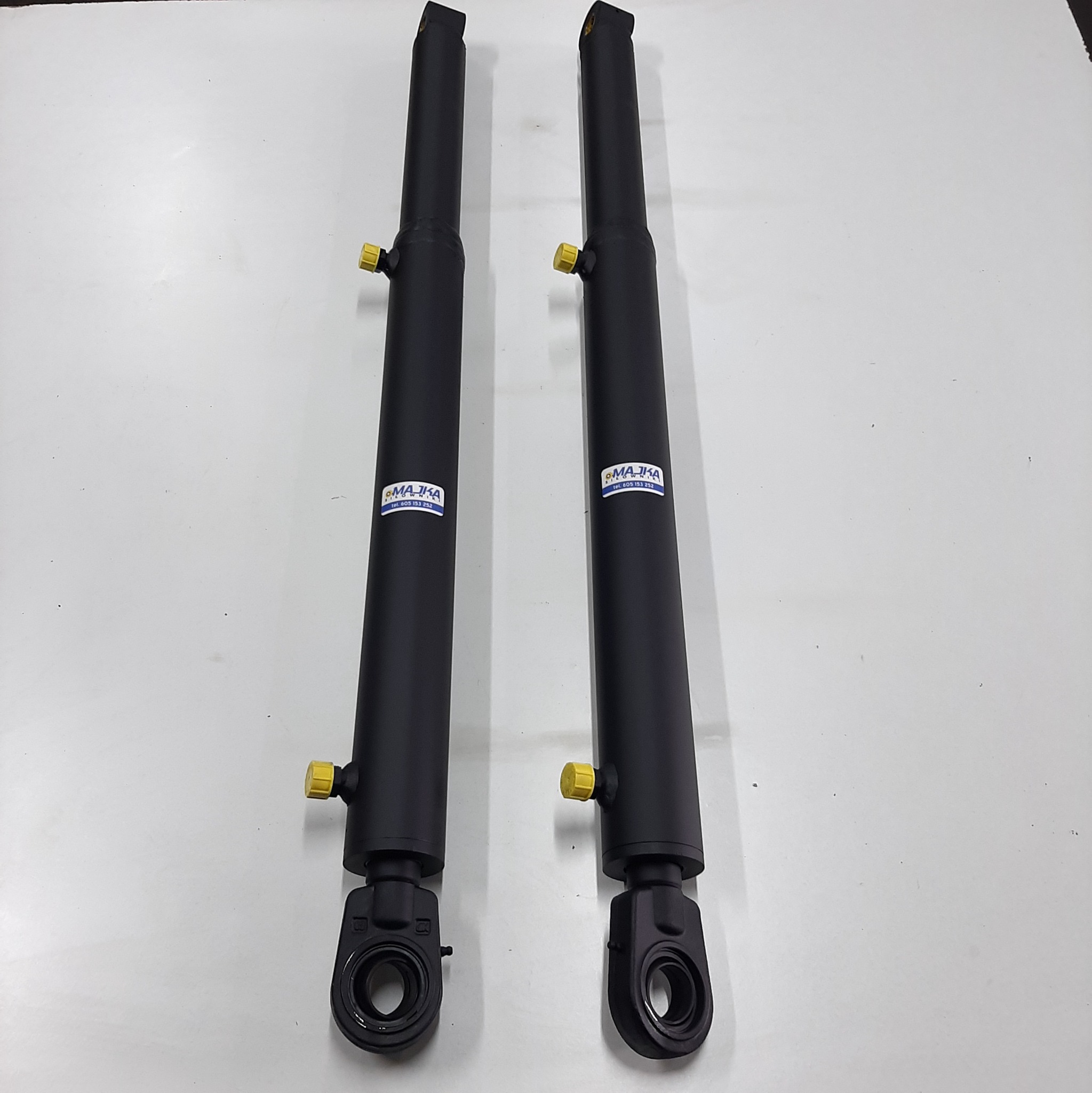 Dwa nowe, czarne siłowniki hydrauliczne z żółtymi zaworami, wyprodukowane w Mierucinku, leżące na białym tle. Widoczne naklejki producenta.