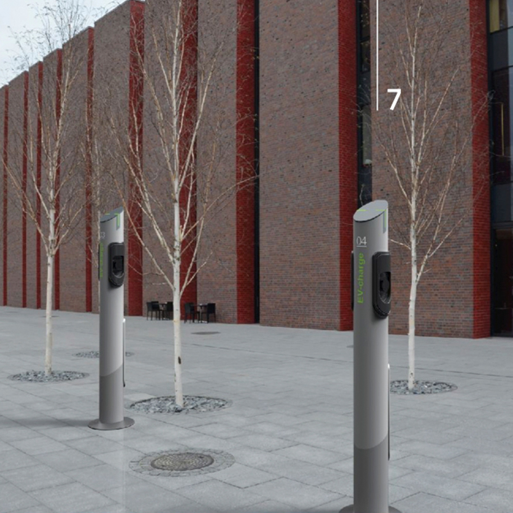 Szare słupki stacji ładowania samochodów elektrycznych z napisem EV-charge na tle ceglanego budynku i drzew w Wodzisławiu Śląskim.