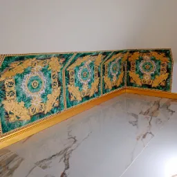 Fragment pomieszczenia z dekoracyjną tapetą w stylu Versace, z motywami roślinnymi i złotymi ornamentami, oraz marmurową podłogą z szarymi żyłami.