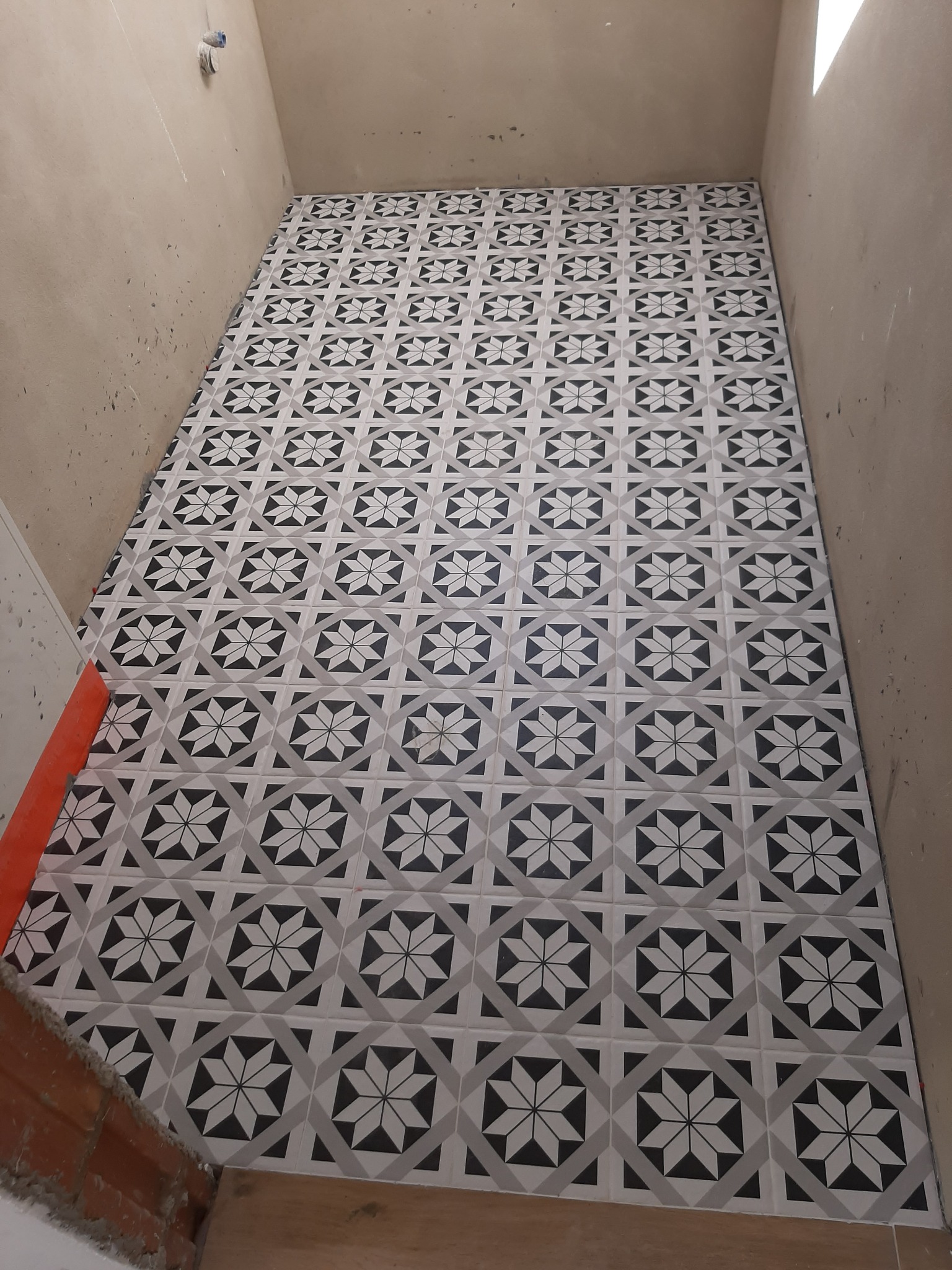 Ułożona podłoga z płytek w geometryczny wzór gwiazdy, świeżo po montażu, widoczne niedociągnięcia na ścianach