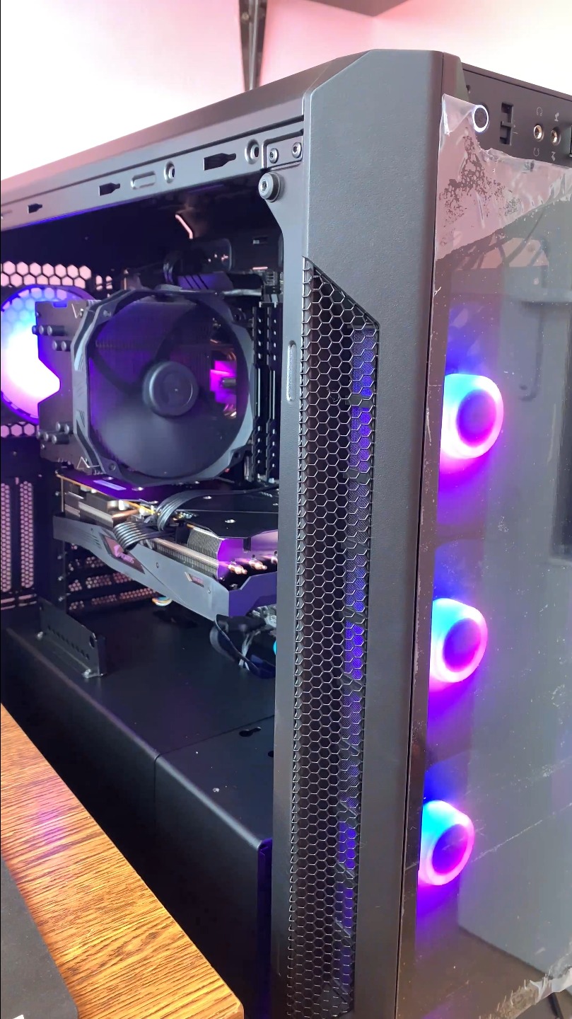 Wnętrze czarnej obudowy komputera stacjonarnego z widocznym chłodzeniem procesora, kartą graficzną Aorus i podświetleniem LED w kolorach fioletu i niebieskiego. Obudowa stoi na drewnianym biurku.