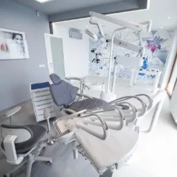 Nowoczesny gabinet stomatologiczny z fotelem dentystycznym, oświetleniem punktowym i geometryczną tapetą w tle.