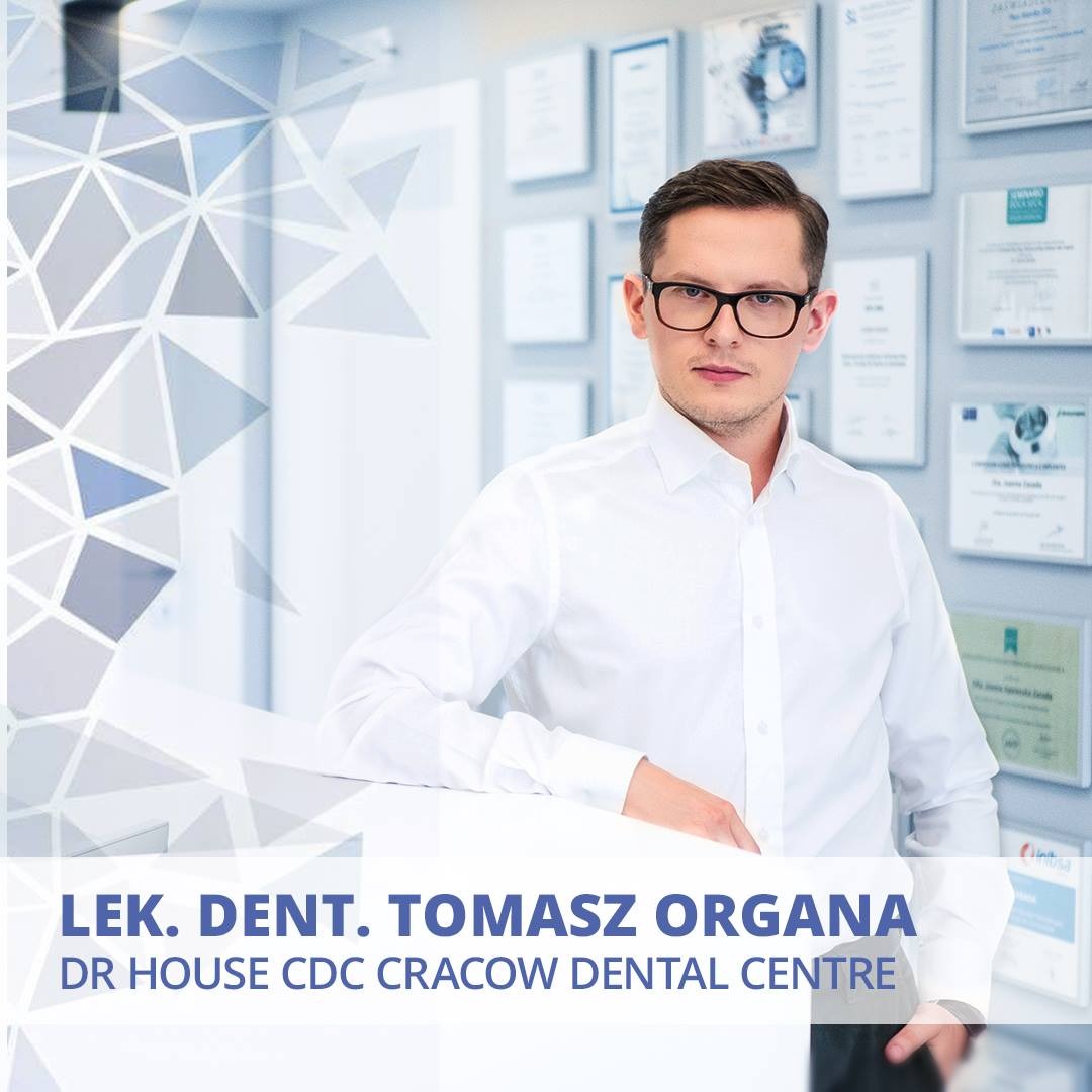 Portret lekarza dentysty Tomasza Organy w okularach, na tle ściany z certyfikatami i dyplomami, w białej koszuli.