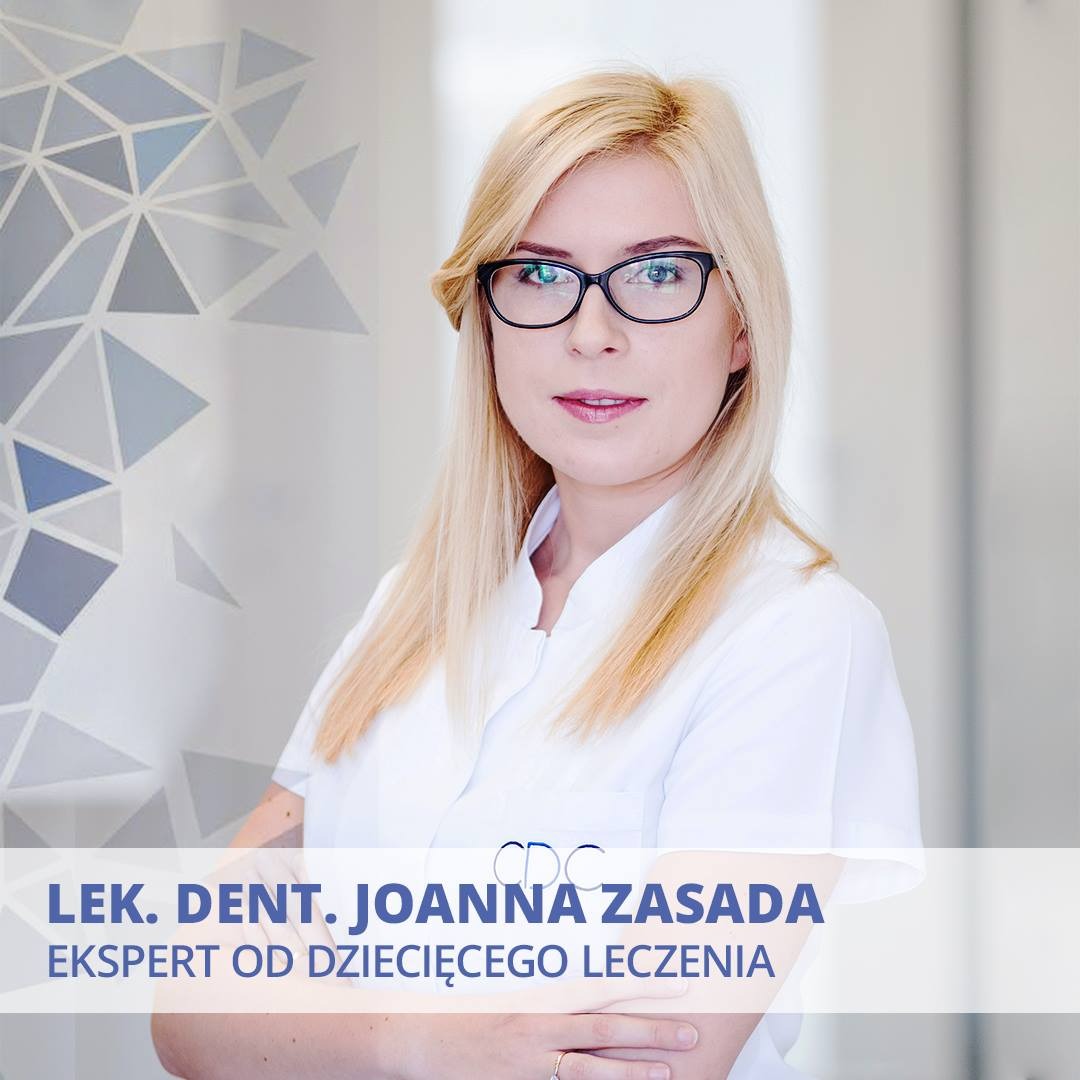 Portret uśmiechniętej lekarki dentystki, Joanny Zasady, w okularach i białym uniformie, na tle ściany z geometrycznym wzorem w odcieniach szarości i błękitu.