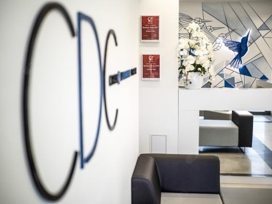 Recepcja kliniki z logo CDC na ścianie, nagrodami i dekoracją z motywem kolibra w tle.