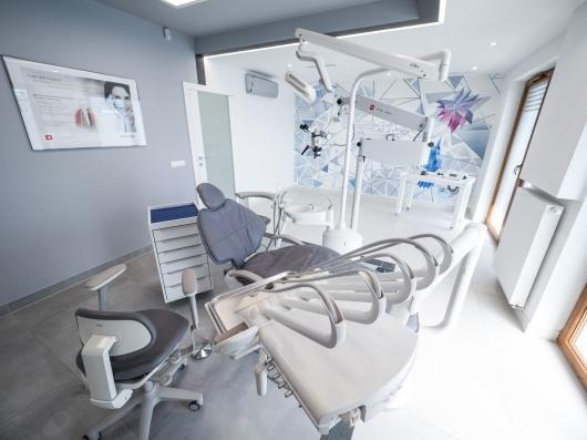 Nowoczesny gabinet stomatologiczny z fotelem dentystycznym, oświetleniem punktowym i geometryczną tapetą w tle.