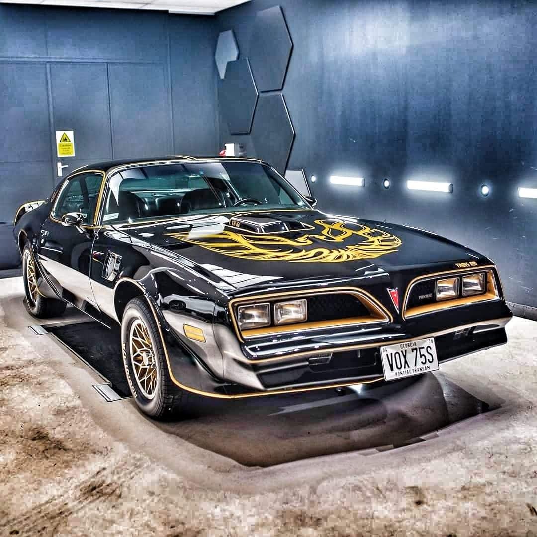 Błyszczący, czarny Pontiac Trans Am z charakterystycznym złotym orłem na masce, zaparkowany w nowoczesnej myjni z dekoracyjnymi panelami na ścianie.