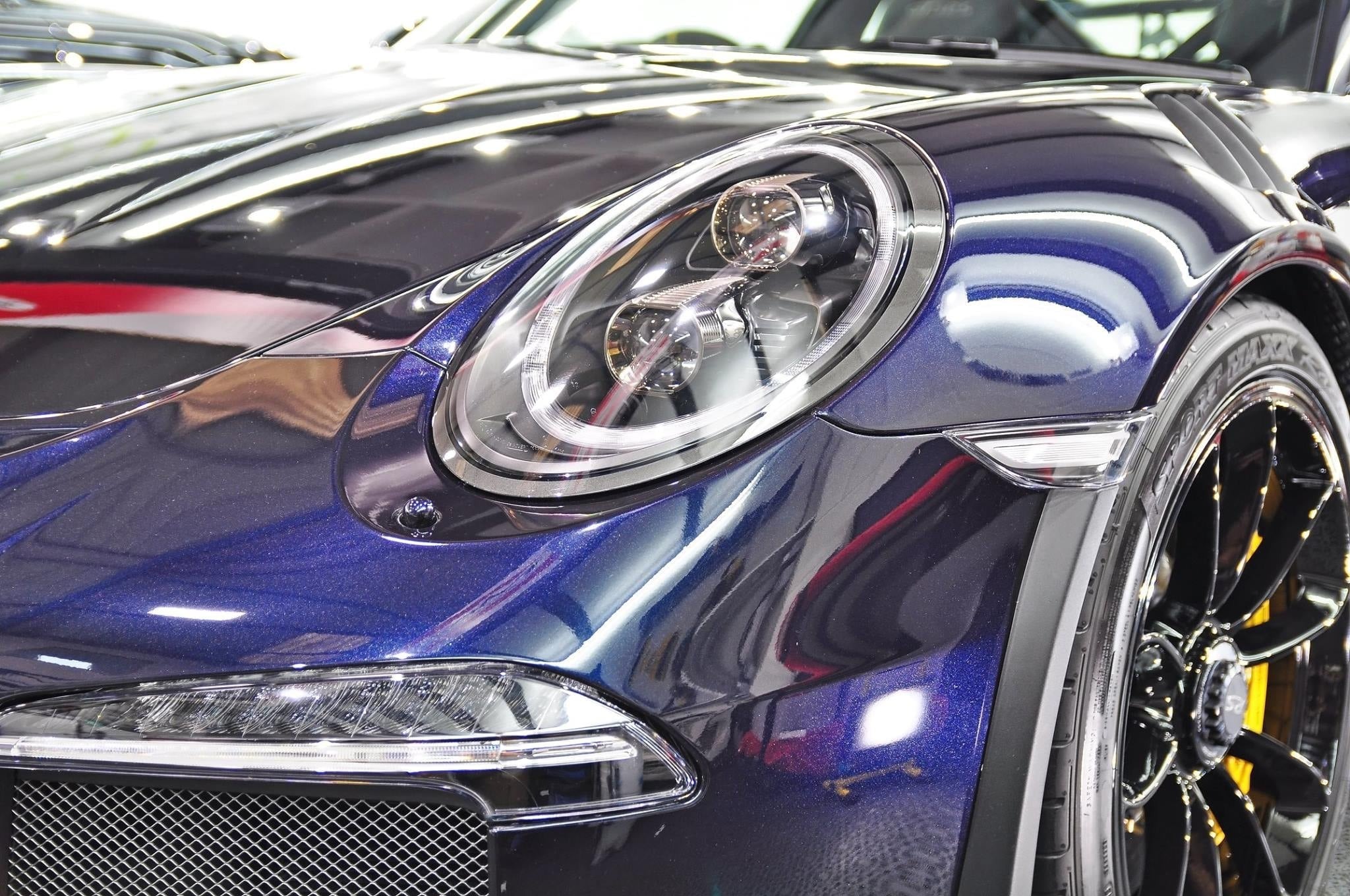Błyszczący, granatowy lakier i reflektor luksusowego samochodu sportowego po detailingu, widoczny grill i felga z oponą.