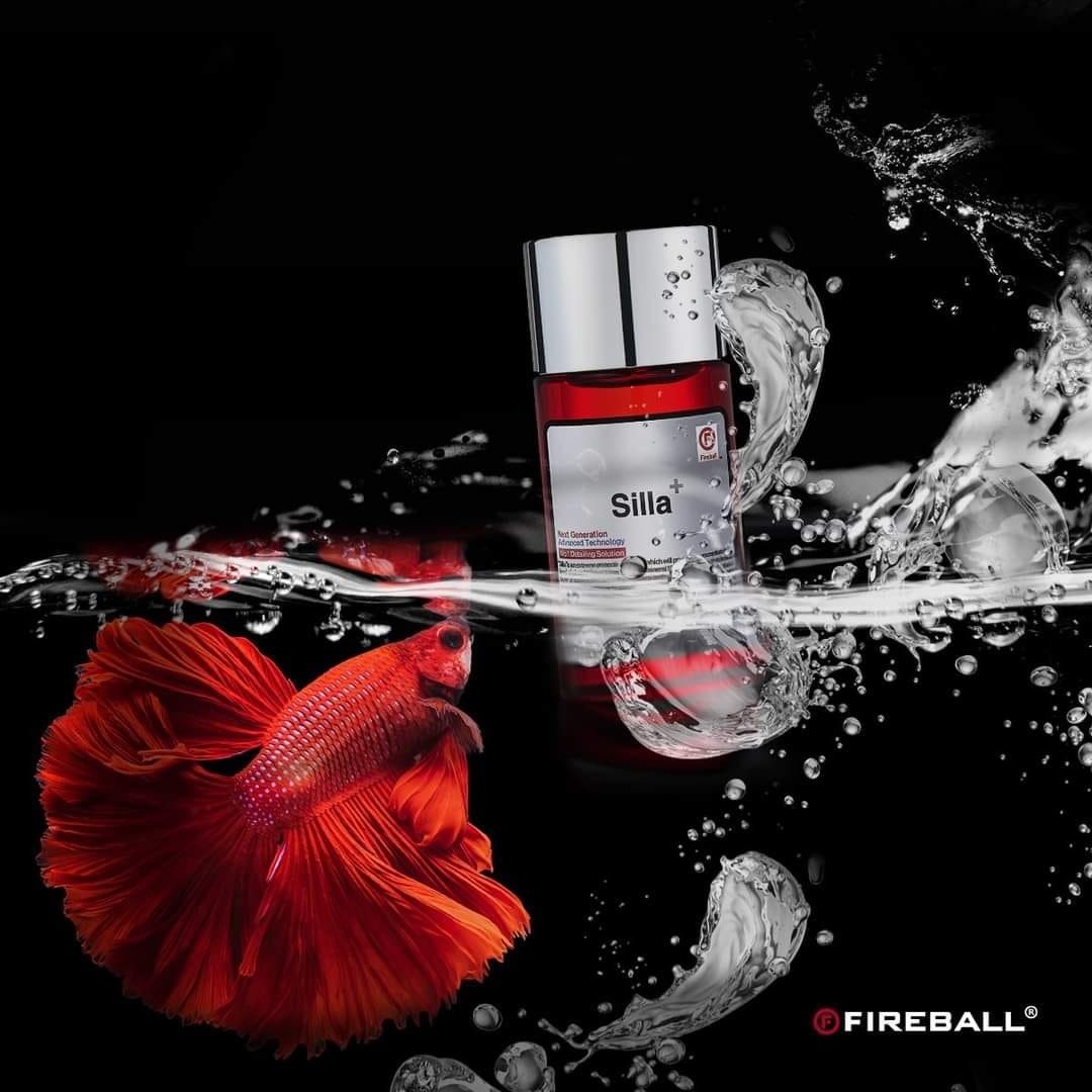 Produkt w czerwonym opakowaniu, częściowo zanurzony w wodzie z pluskającą się wodą i czerwonym bojownikiem syjamskim, na czarnym tle, z widocznym logo Fireball.