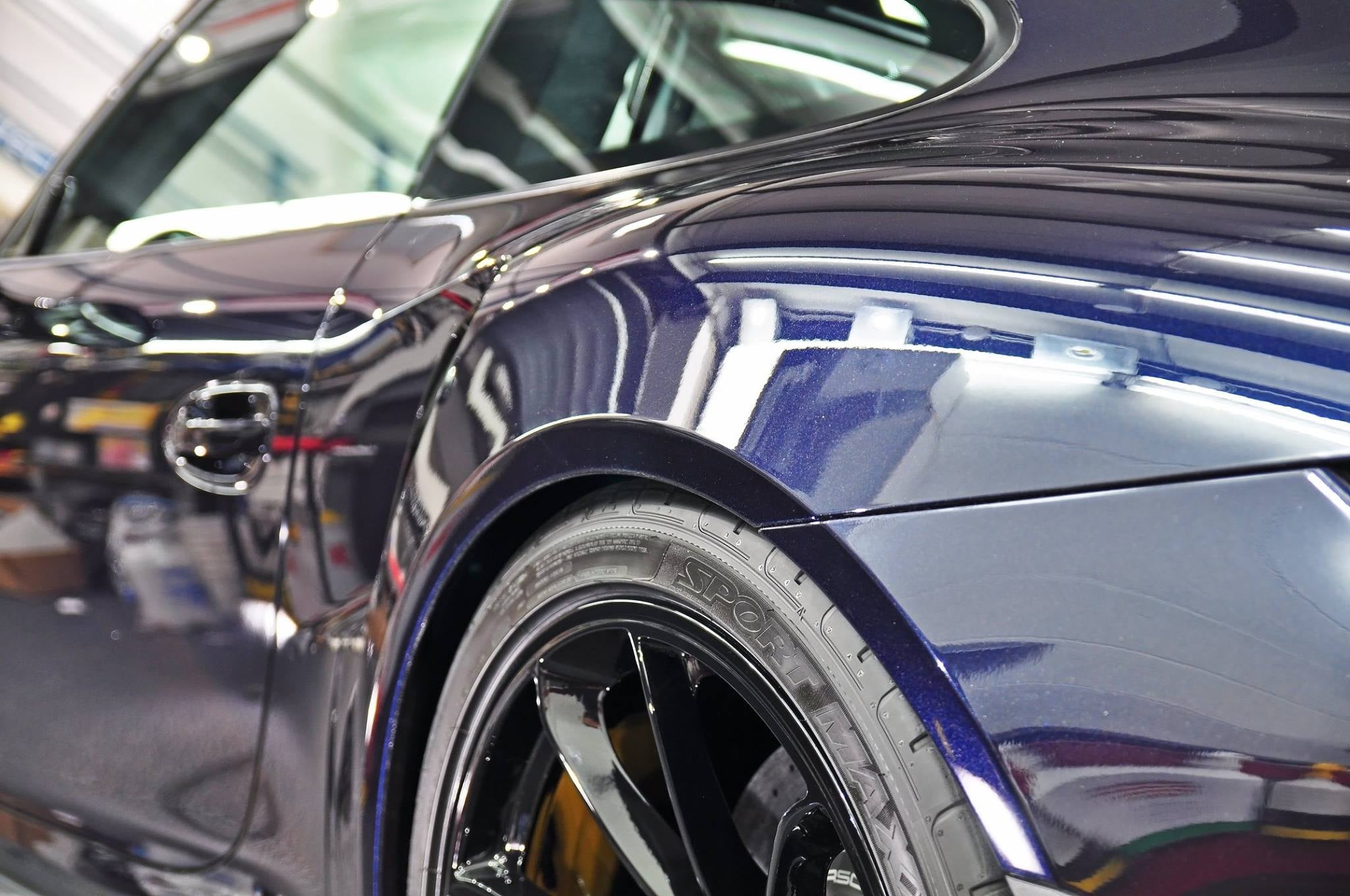 Błyszczący, granatowy samochód sportowy po umyciu, z widocznym detalem opony i felgi, odbijający światła w lakierze.