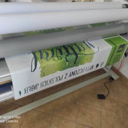 Raster Michał Jordan - Proces laminowania wydruku wielkoformatowego z motywem jabłek i napisem 'Wy tłoczony z polskich jabłek' na maszynie drukarskiej.