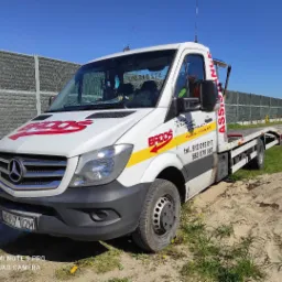 Biała laweta Mercedes z czerwonym logo 'BADOS' zaparkowana na piaszczystym podłożu obok drogi, z widocznym numerem telefonu kontaktowego i adresem firmy na karoserii.