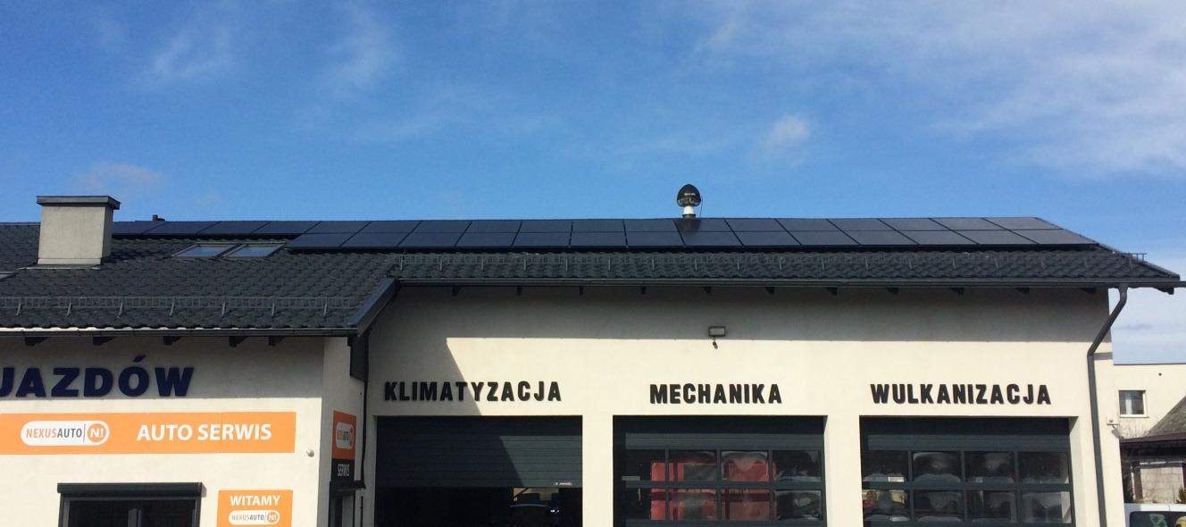 Panele słoneczne na dachu budynku warsztatu samochodowego z napisem: Klimatyzacja, Mechanika, Wulkanizacja.