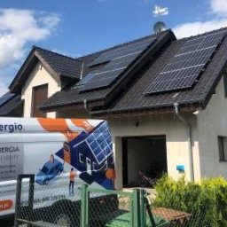 Synergio Spółka Akcyjna - Dom jednorodzinny z panelami słonecznymi na dachu, widoczny z boku samochód firmowy z reklamą instalacji fotowoltaicznych.