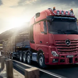 Czerwony ciągnik siodłowy Mercedes-Benz Actros GigaSpace z naczepą przewożący betonowe bloki na tle górskiego krajobrazu, widok z przodu, w ruchu.