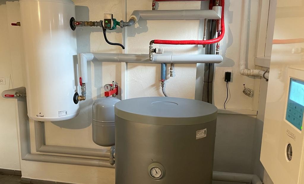 Instalacja kotłowni z dwoma zbiornikami, rurami w izolacji termicznej i panelem sterowania, widoczne manometry i zawory.