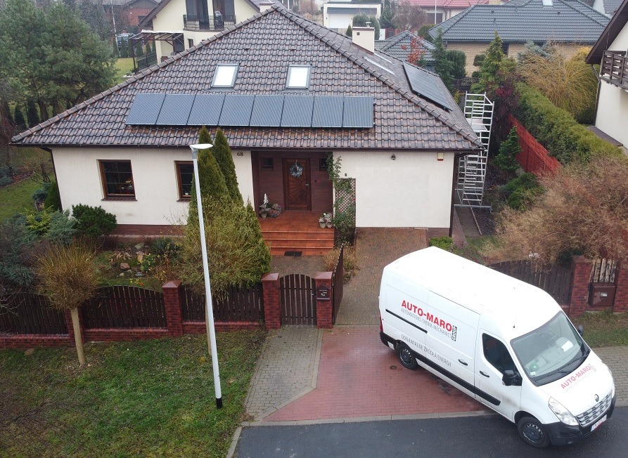 Dom jednorodzinny z panelami słonecznymi na dachu, widok z góry, na podjeździe biały samochód dostawczy z logo firmy, rusztowanie oparta o ścianę budynku.