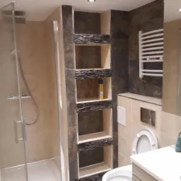 Nowoczesna łazienka z kabiną prysznicową, toaletą, umywalką i wnękami ściennymi wykończonymi kamieniem dekoracyjnym, oświetlona punktowo.