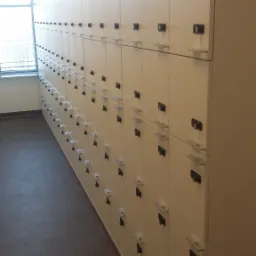 Rząd jasnych szafek z zamkami szyfrowymi w jasnym pomieszczeniu z oknem.