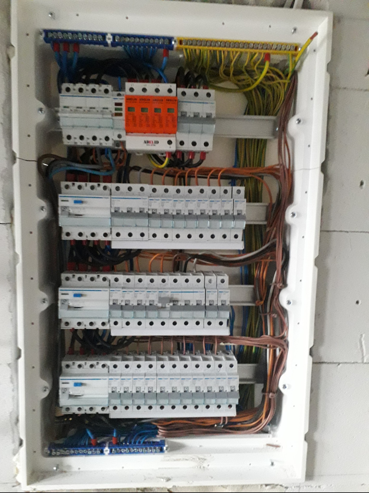 Rozdzielnica elektryczna z zabezpieczeniami przepięciowymi i przewodami w ścianie budynku w Wałczu, widoczne liczne bezpieczniki i listwy zaciskowe.