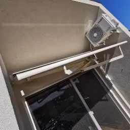 Biała jednostka zewnętrzna klimatyzacji marki Whirlpool zamontowana na ścianie budynku obok zwiniętej markizy nad oknem.