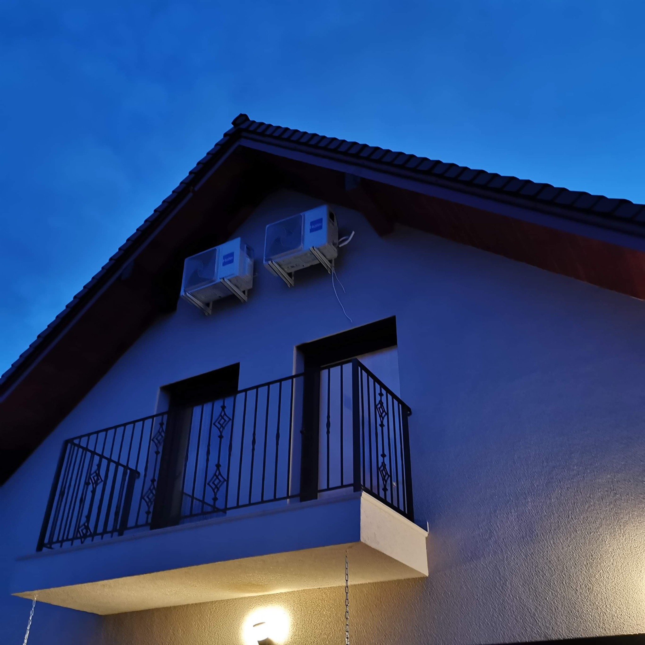 Dwa klimatyzatory Haier zamontowane na elewacji domu z balkonem, widok nocny, przewody elektryczne widoczne.