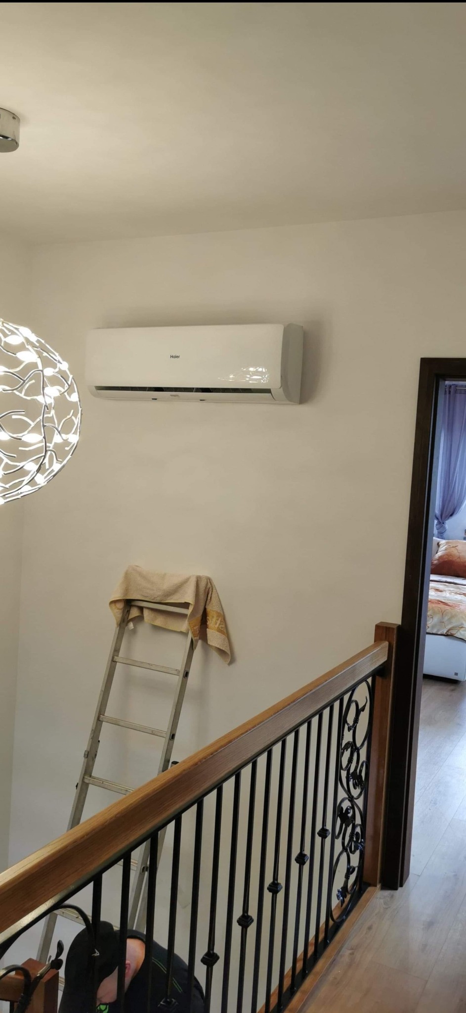 Zamontowana jednostka klimatyzacji Haier w jasnym wnętrzu w Legnicy, drabina oparta o ścianę z ręcznikiem, widok zza ozdobnej balustrady schodów.