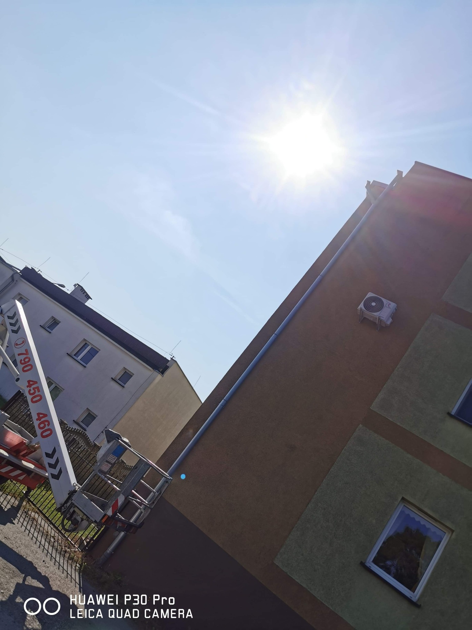 Montaż jednostki zewnętrznej klimatyzacji na elewacji budynku z wykorzystaniem podnośnika koszowego w słoneczny dzień.