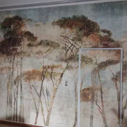 Fototapeta z motywem drzew w stylu malarskim zdobiącą ścianę w pokoju, widoczna rama drzwi i gniazdka elektryczne.