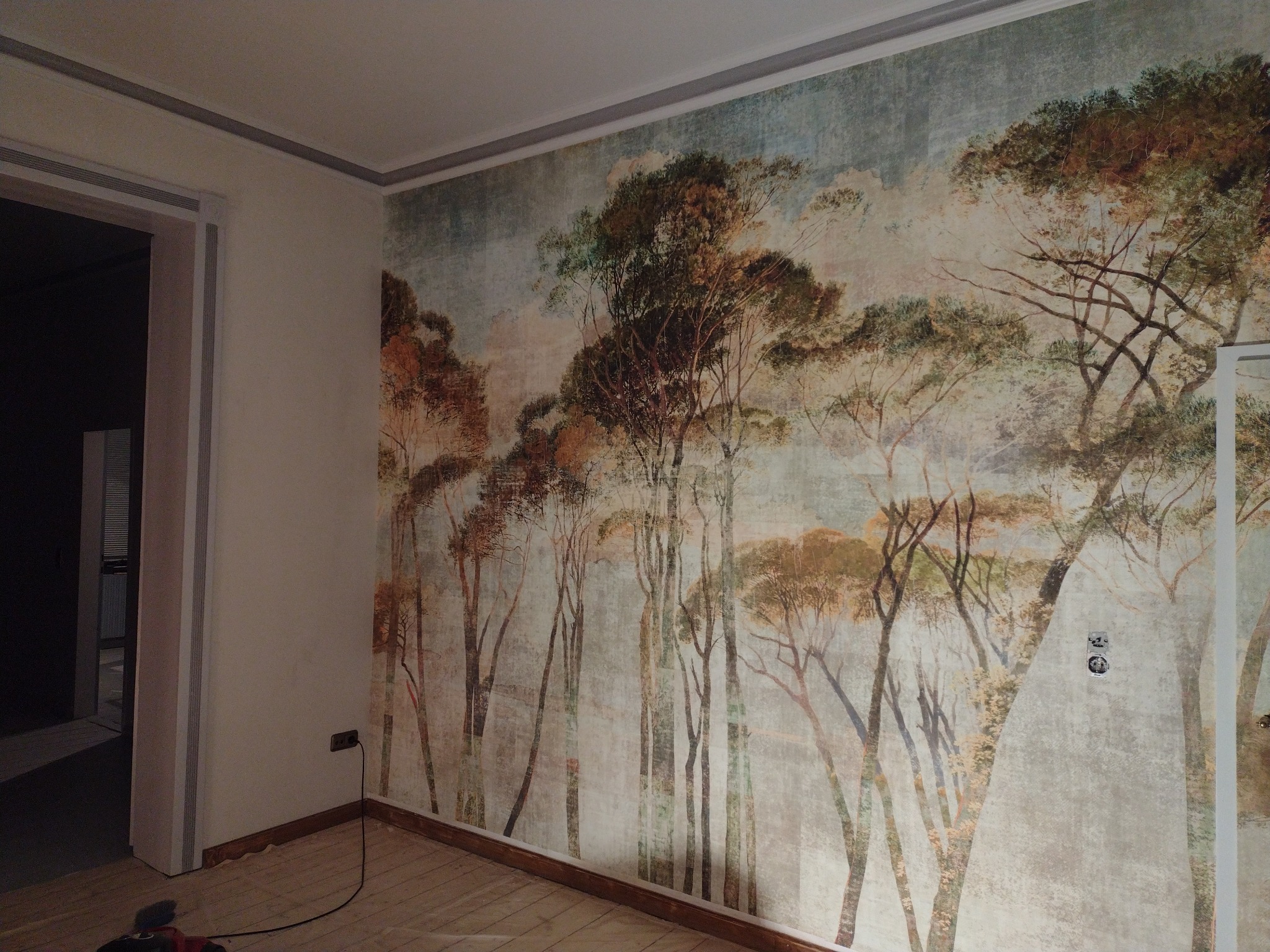 Pokój z fototapetą przedstawiającą las, widoczne gniazdka elektryczne na tle wzoru.