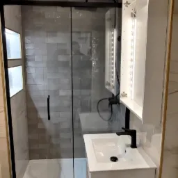 Nowoczesna łazienka z kabiną prysznicową typu walk-in z czarną ramą, białą szafką umywalkową z czarną armaturą i podświetlaną szafką lustrzaną.