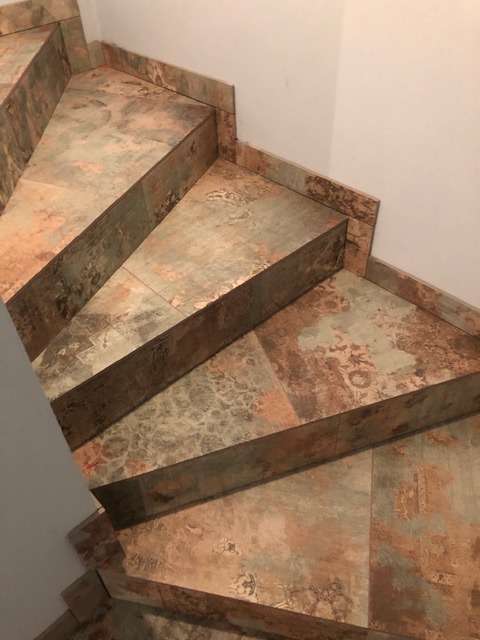 Schody wyłożone płytkami ceramicznymi imitującymi wzór dywanu, z detalami dekoracyjnymi i bordiurą na krawędziach stopni.